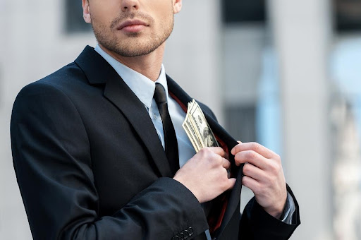 A man in a suit hiding money in an inside pocket, representing white-collar crime